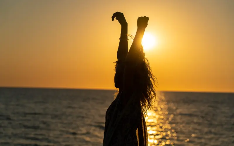 Moteris, šokanti laisvu judesiu prieš saulėlydį, simbolizuojanti vidinę bangą